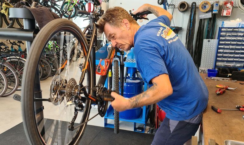 A man is focused on fixing a bicycle in a garage filled with various tools and equipment.