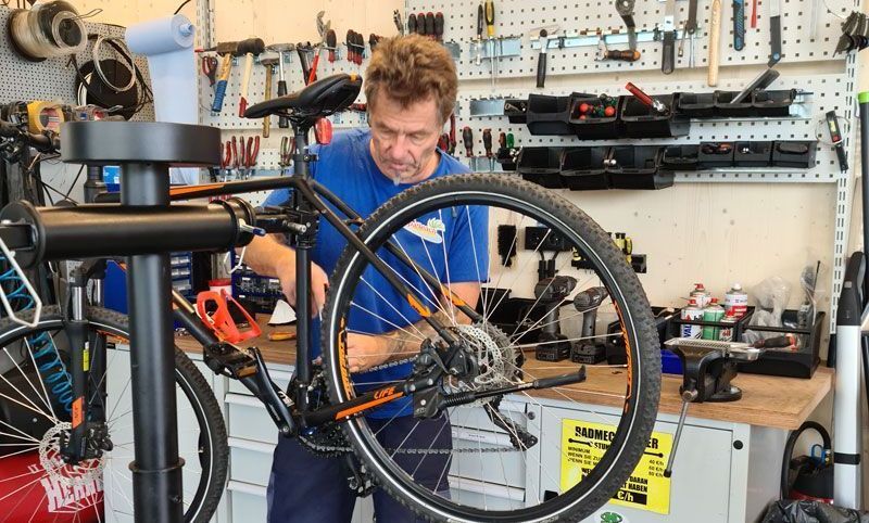 A man is focused on fixing a bicycle in a garage filled with various tools and equipment.